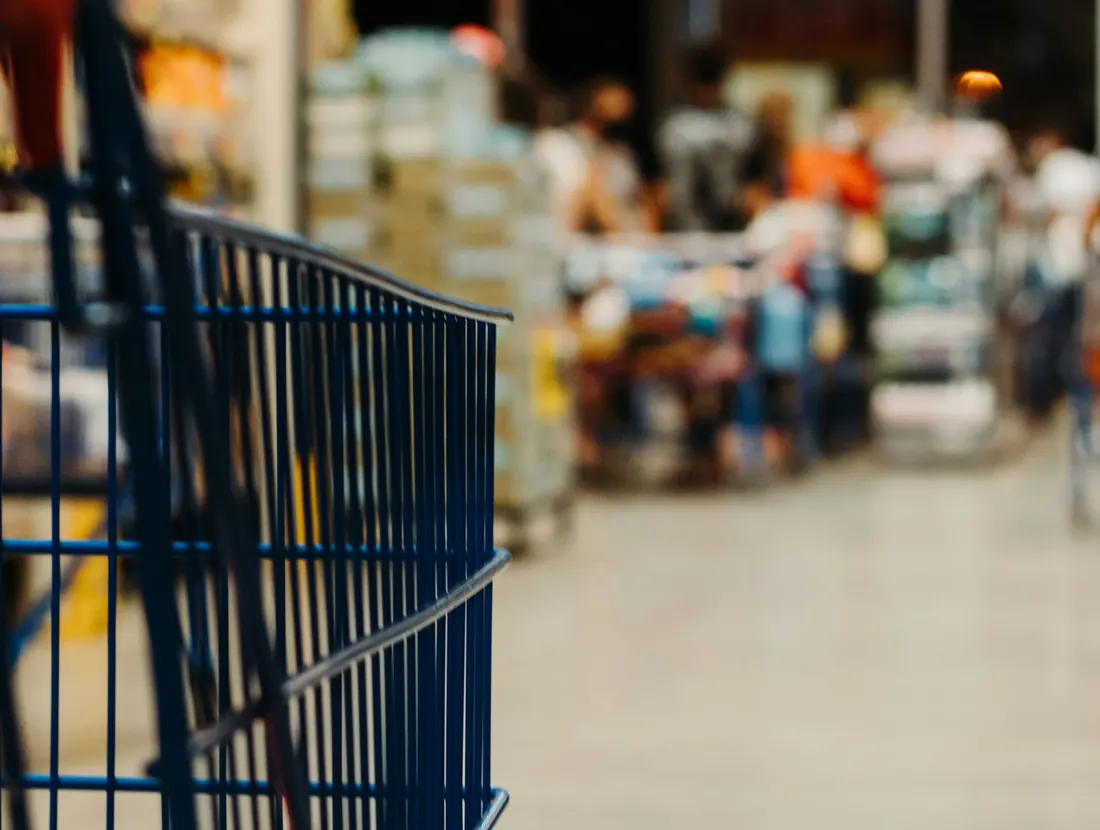 Shopping trolley in a supermarket aisle stocked with packaged goods